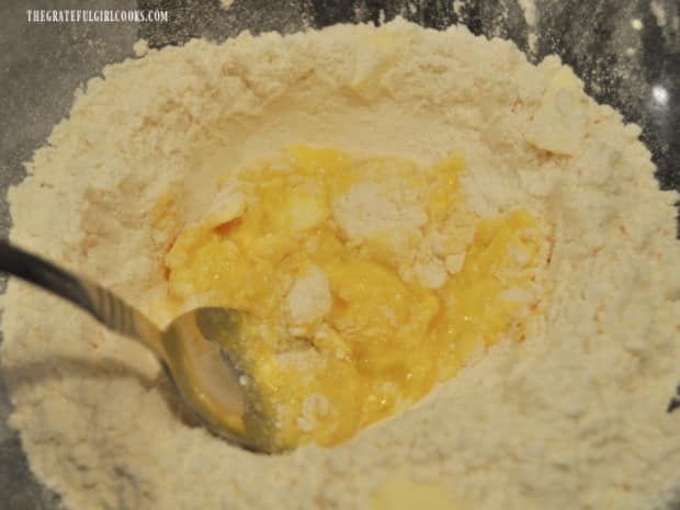 An egg and cold pieces of butter are added to the flour mixture in a large bowl to make dough.