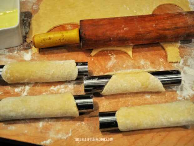 Four cannoli tubes are wrapped and seams are sealed with egg white before frying.