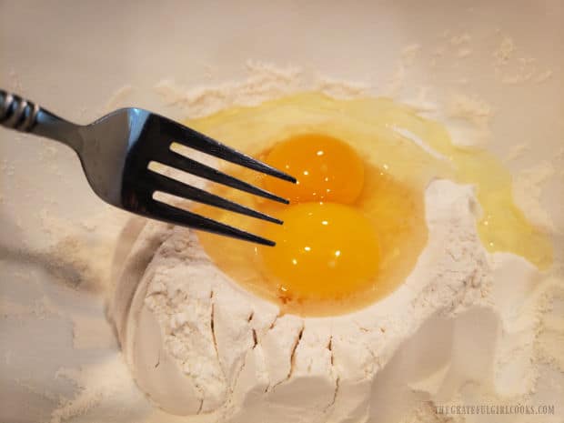 Two eggs are added to the well in flour and salt mixture, and a fork is used to combine them.