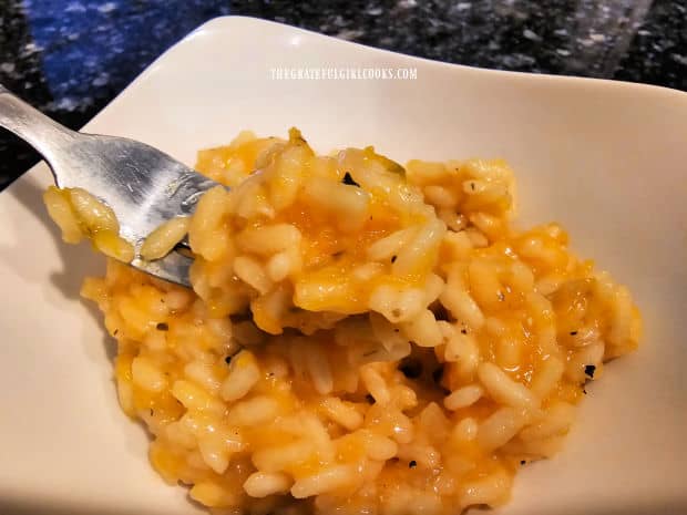 A fork lifting out a bite of the pumpkin risotto from a white bowl.