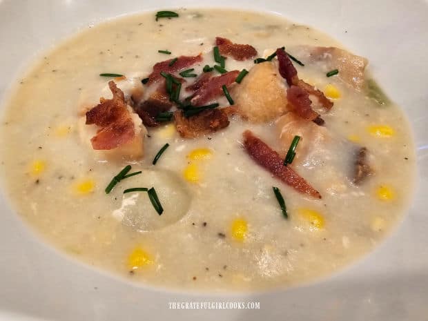 A bowl of rockfish potato chowder is served with bacon/chive garnish.