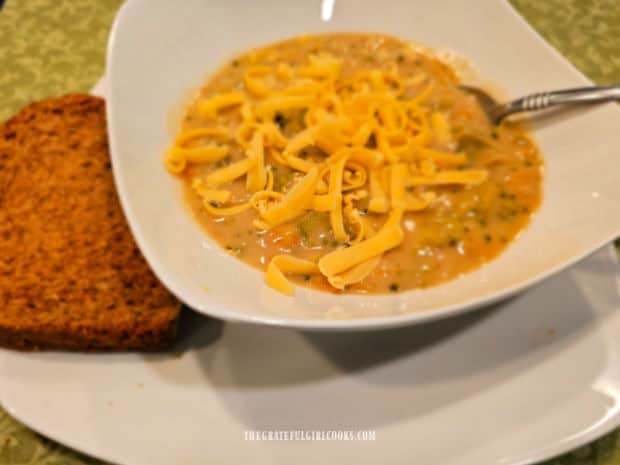 Bowl of broccoli cheese soup topped with cheese, and bread on the side.