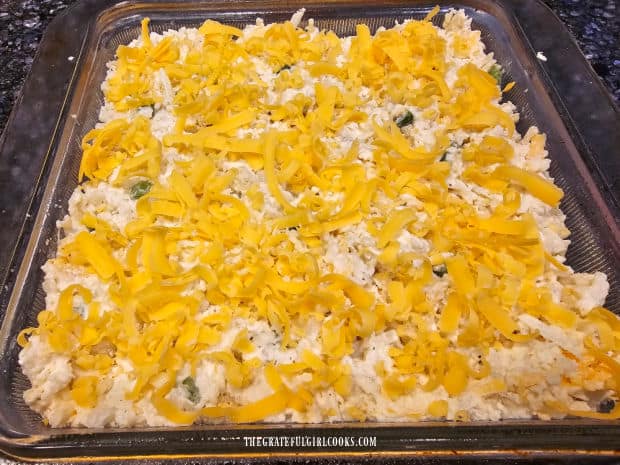 Shredded cheddar cheese is sprinkled on top of the casserole before baking.