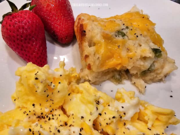 A piece of cheesy hash brown casserole, served with eggs and strawberries.