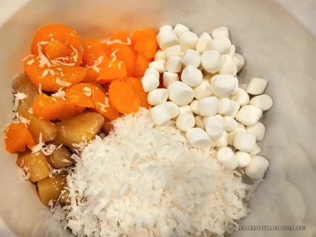 Mandarin oranges, pineapple, coconut and mini marshmallows, in a bowl.