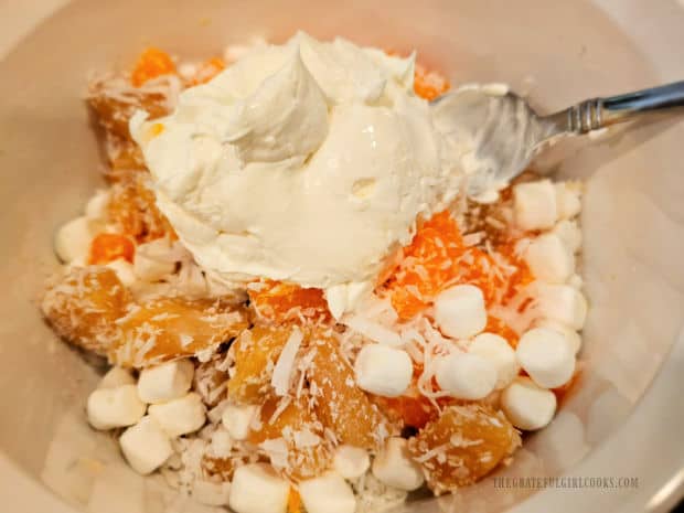 Sour cream is added to the fruit salad in the bowl.