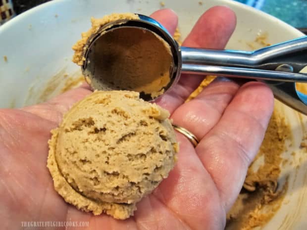 Cookie dough is scooped out and rolled into a ball.