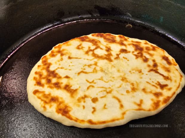 Naan bread is flipped halfway through cooking, revealing browned surface.