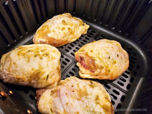 marinated chicken thighs are place in air fryer basket for cooking.