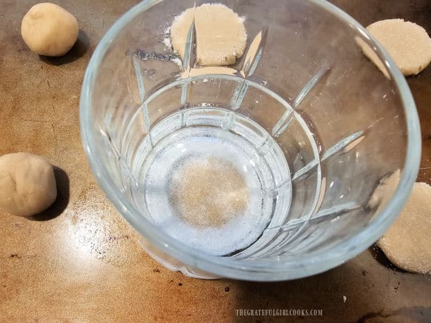 Sugar-coated bottom of a glass is pressed onto cookie dough balls to flatten.