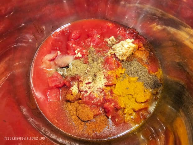 Spices and diced tomatoes are placed in the inner pot of a pressure cooker.