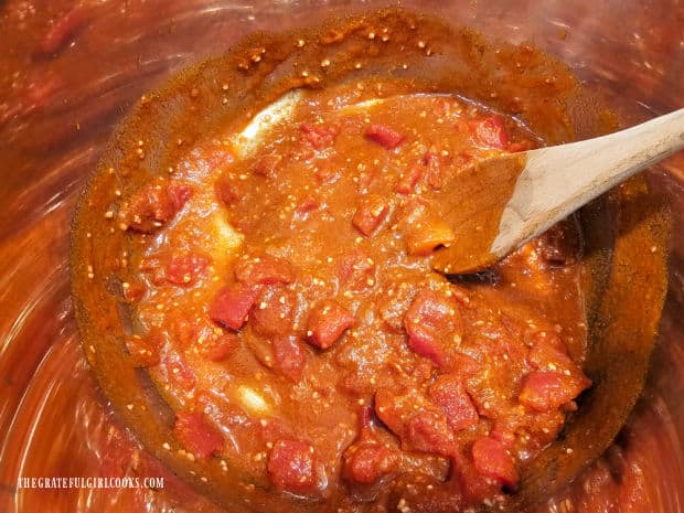 Tomatoes and spices are stirred until fully combined in inner pot.