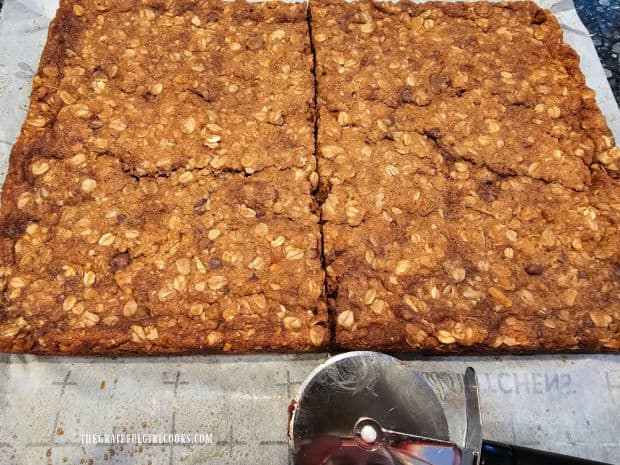 Baked granola bars are cut in half using a pizza cutter.