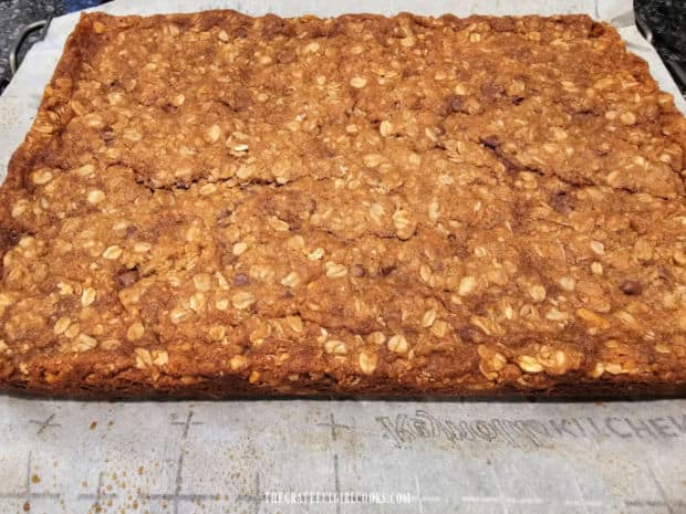 Baked granola bar dough cools on parchment paper on a wire rack.