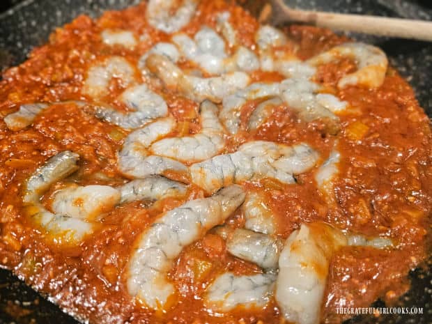 Shrimp are placed in the skillet of Creole sauce in a single layer.