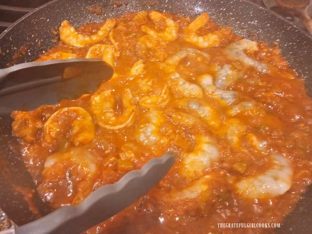 Tongs are used to flip the shrimp to cook the other side in the sauce.