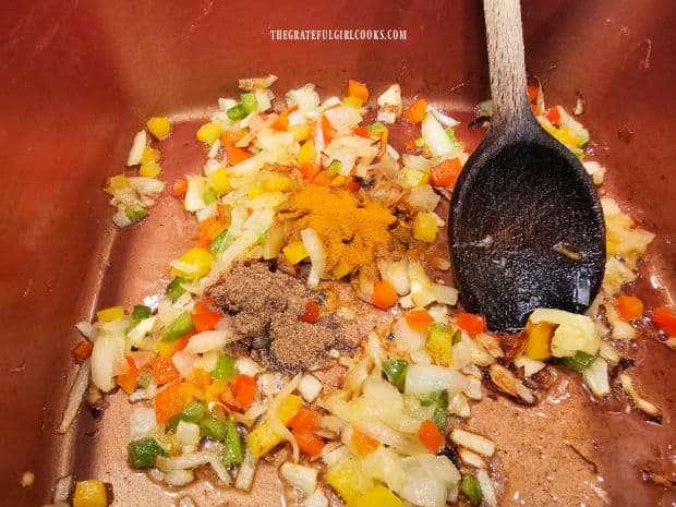 Ground cumin and ground turmeric are added to cooked veggies in pan.