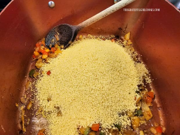 Uncooked couscous is added to the saucepan of seasoned veggies.