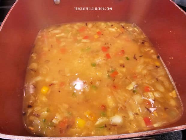 Hot chicken broth is added to the couscous and veggies in pan.