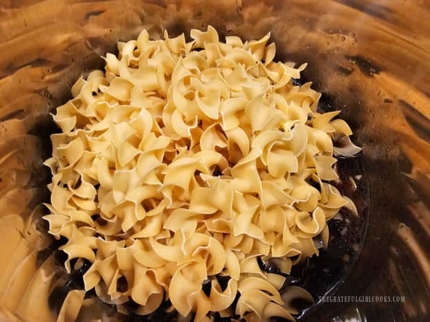 Uncooked egg noodles are added and stirred into the broth.