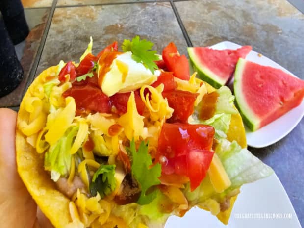 Holding a tostada, with a plate of watermelon slices in the background.