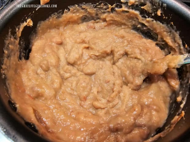 Refried beans and water are heated in a small saucepan.