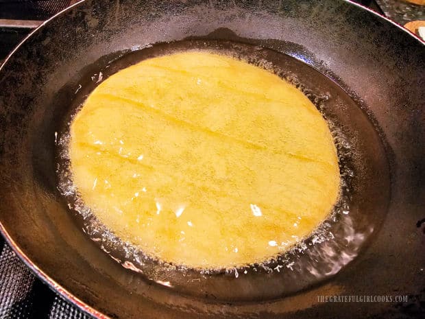 A corn tortilla is placed in hot oil and fried until crisp.