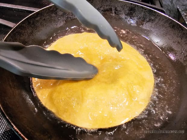 Tongs are used to press center of tortilla down into hot oil for crispness.