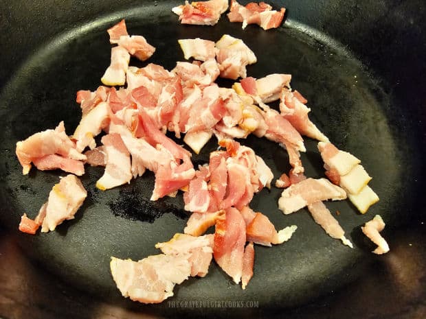 Chopped pieces of bacon are cooked in a large cast iron skillet.