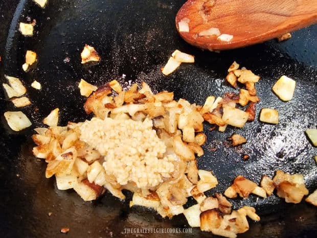 Minced garlic is added to the caramelized onions in the skillet and cooked.