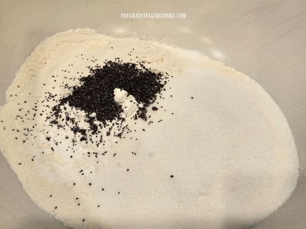 Flour, sugar, baking powder, salt and poppyseeds in a large, white bowl.