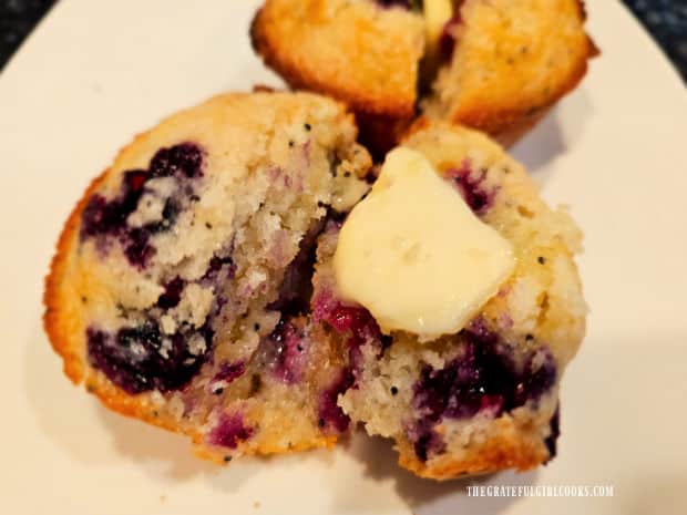 Butter inside warm blueberry lemon poppyseed muffins, on a white plate.