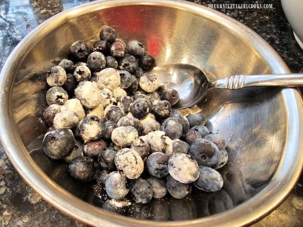 Fresh blueberries are coated with flour in a bowl.