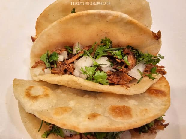 Instant Pot Pork Carnitas are served in taco shells, with onions and cilantro.