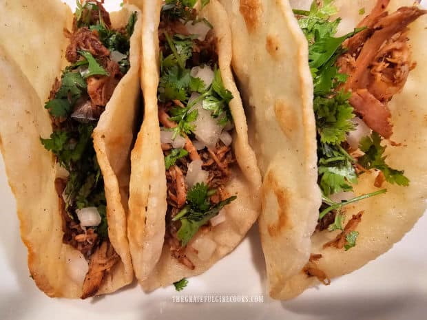 Three of the Instant Pot Pork Carnitas with onions and cilantro on a plate.