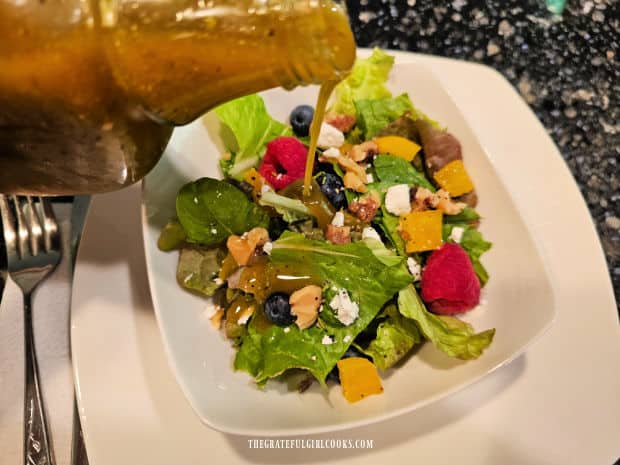 Some of the Italian Vinaigrette is poured onto a mixed green salad.