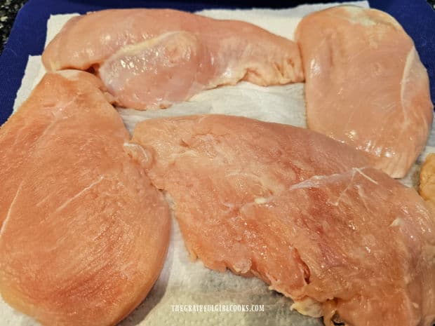 Boneless, skinless chicken breasts are blotted dry using paper towels.