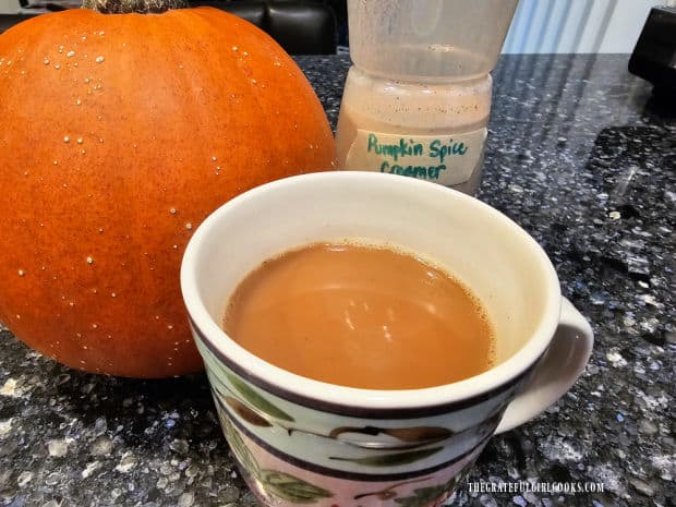 A pumpkin, and a cup of coffee with pumpkin spice creamer in it.