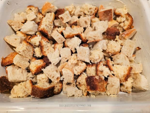 Stale bread cubes are place in a buttered baking dish.