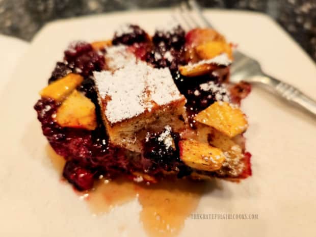 A piece of Blackberry Apple French Toast Bake, with powdered sugar and syrup.