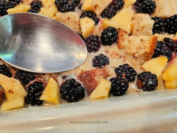 Fruit and bread are pressed down into egg mixture using the back of a spoon.