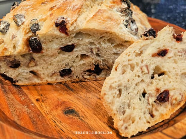 A slice of the bread is cut, revealing cranberries and pecans inside the loaf.