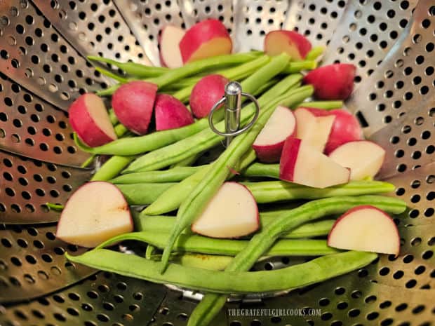 Whole green beans and cubed red potatoes in a steamer basket.