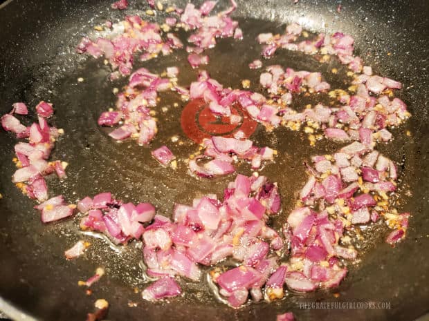 Chopped red onion and garlic are cooked in olive oil in a large skillet.