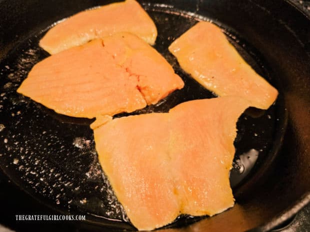 Salmon cooking in a large cast iron skillet, sauce side down.