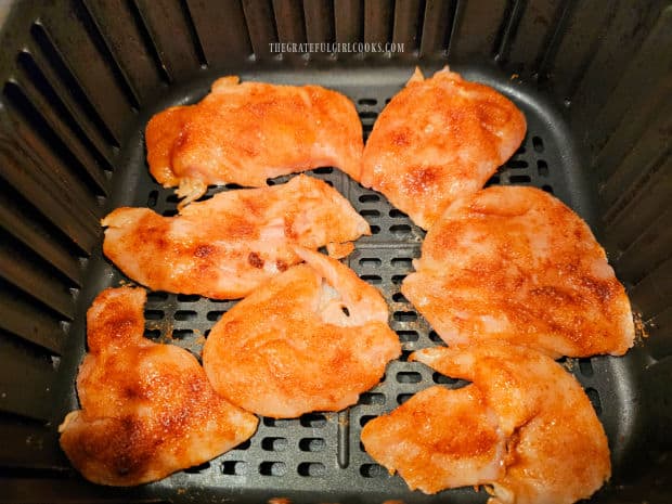 Seasoned chicken pieces in air fryer in single layer for cooking.