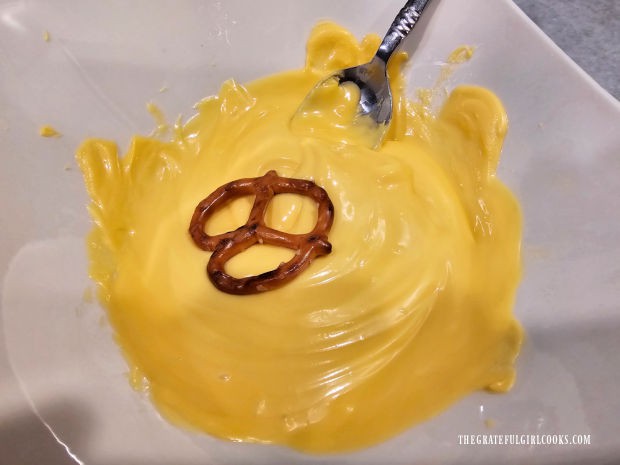 A pretzel is being dipped in yellow melted chocolate candy wafers.