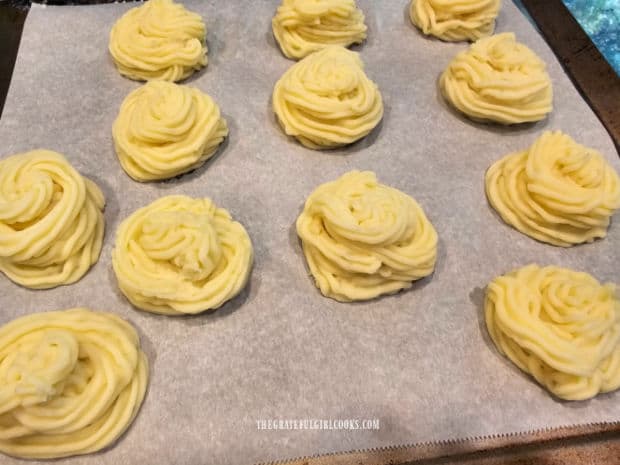 Swirls of Duchess potatoes on parchment paper-lined baking sheet.