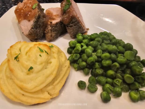 Duchess potatoes, on a white plate with pork tenderloin slices and green peas.