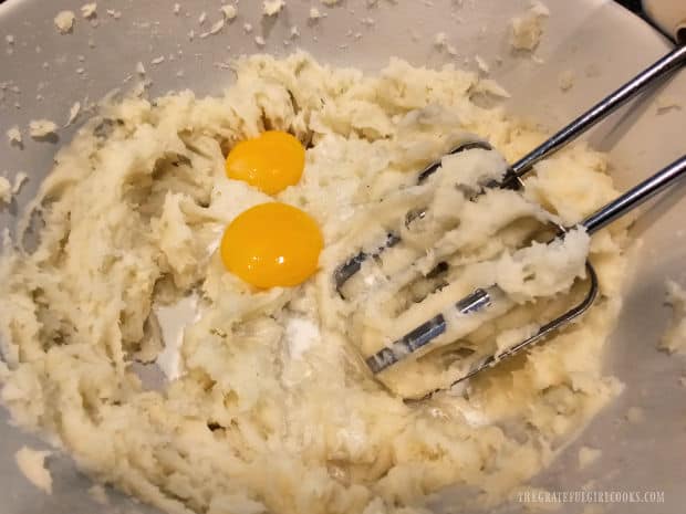 Two egg yolks and half and half are added to mashed potatoes in bowl.